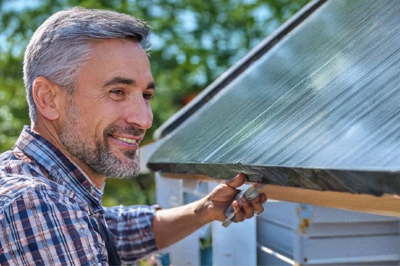Heimwerker, der Dachfolie auf einer Gartenhütte verlegt